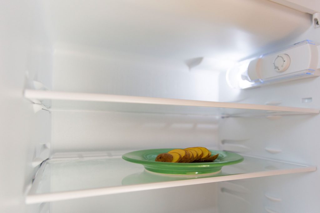Teller mit Kartoffelscheiben in leerem Kühlschrank