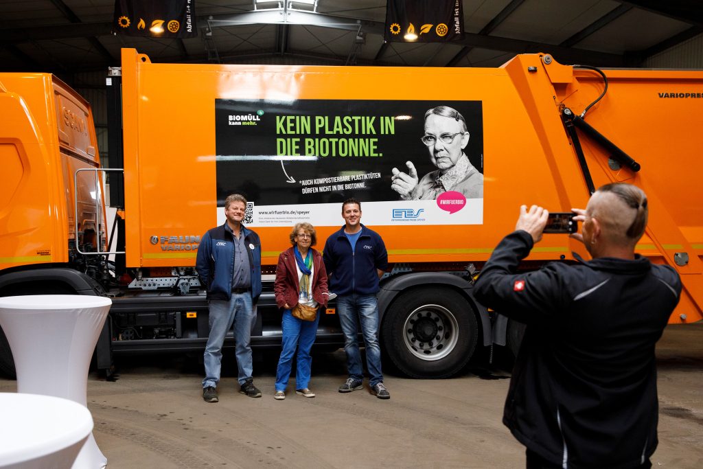 Drei Personen stehen vor Müllfahrzeug mit #wirfuerbio-Motiv "Kein Plastik in die Biotonne"